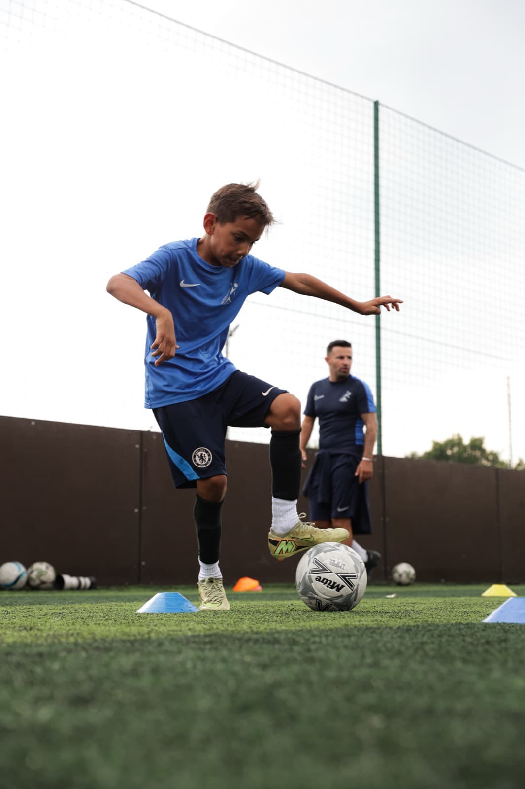 Young player practising a skill move while a coach watches